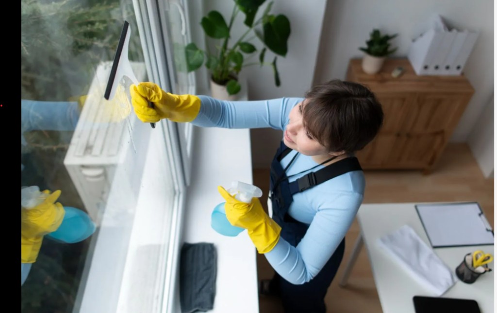 Professional cleaning a large interior window with squeegee and spray